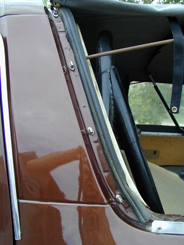 1979 Ford Bronco - Close-up of the rear quarter panel of a glossy maroon truck body where a gray soft top's edge is snapped to a row of studs along the bed ra…
