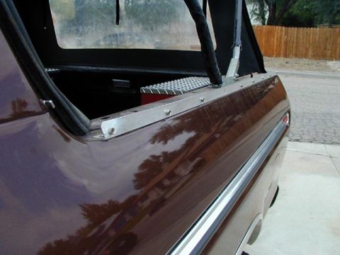 1979 Ford Bronco - Close-up along the glossy maroon bedside of a truck showing a bare aluminum mounting strip screwed to the top of the bed rail with a soft-t…
