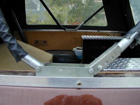 1979 Ford Bronco - Rear cargo area of a soft-top SUV shot over the tailgate, showing bare plywood bulkhead panels, a rubber floor mat and diamond-plate alumin…