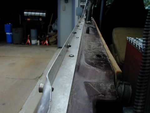 1979 Ford Bronco - Low-angle view down the length of a maroon truck bed rail, showing a bare aluminum trim strip and a row of soft-top snap studs running alon…