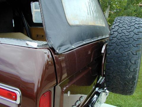1979 Ford Bronco - Rear quarter close-up of a brown Ford Bronco with a black vinyl soft top snapped along the body line and a diamond-plate trim strip on the…