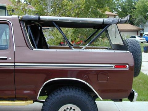 1979 Ford Bronco - Maroon full-size Ford Bronco, side profile with soft-top removed and bows folded, chrome trim, spare tire and large tires, parked on a stre…