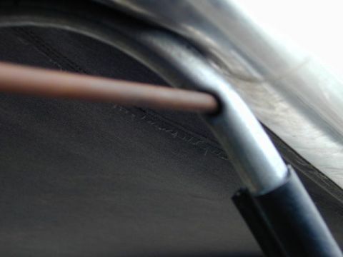 1979 Ford Bronco - Extreme close-up of a bare steel rod meeting a bent tubular soft-top bow, with the rod end slotted into a welded tab on the bow. Dark fabri…