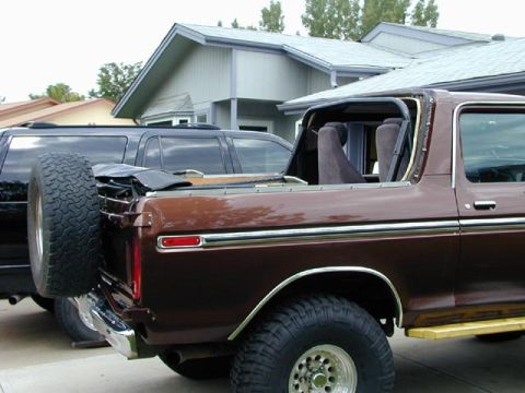 1979 Ford Bronco - Dark brown Ford 4x4 with its hardtop and bed cap partially removed, parked beside a black truck in a residential driveway.