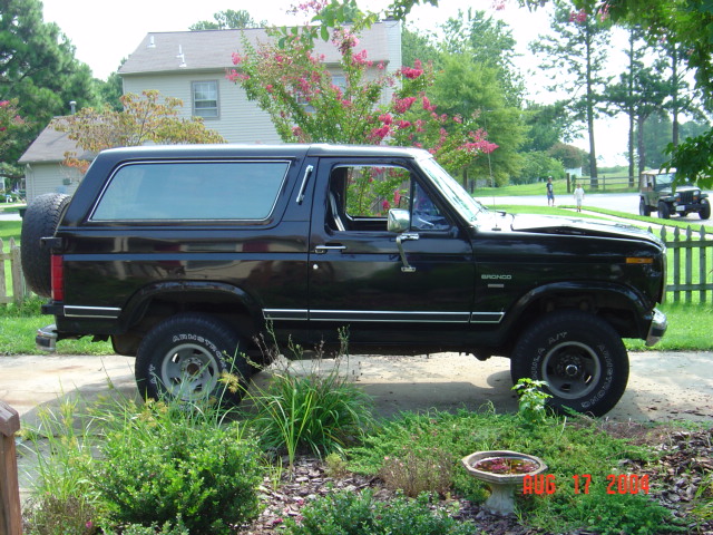 Side view of a lifted black Ford Bronco SUV on steel wheels parked in a driveway near a garden and house