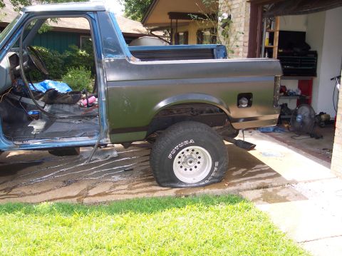 1990 Ford Bronco - This SUV, possibly a Ford Bronco, is in a state of disrepair with a flat tire and missing door.