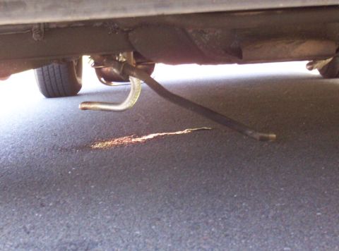 1991 Ford Crown Victoria LTD - A vehicle's undercarriage is visible, with a bent pipe and a fluid leak on the asphalt.