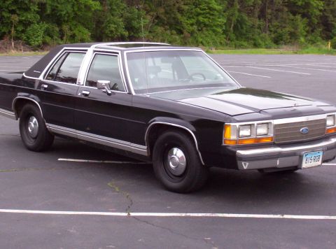 1991 Ford Crown Victoria LTD - This black Ford Crown Victoria is parked in an empty lot with trees in the background.