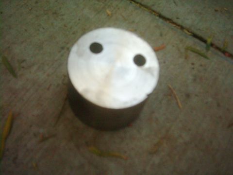 1978 Ford Bronco - A piston with two holes that give it a face-like appearance sits on a concrete surface.