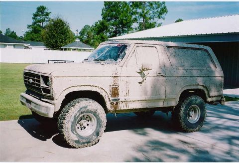 1984 Ford Bronco - This heavily soiled Ford Bronco, likely from the early 1980s, is viewed from the front three-quarter angle.