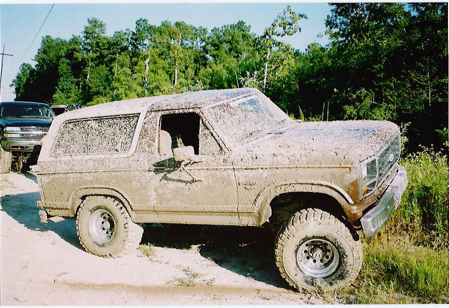 Mud-covered 1984 Ford Bronco, 3/4 front view, with another SUV behind it