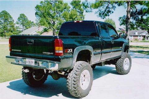 1984 Ford Bronco - A black Chevrolet Silverado pickup truck is shown from a rear three-quarter angle, modified with a lift kit and off-road tires.