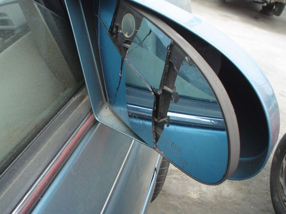 Blue car side mirror with cracked and broken glass, viewed from the door