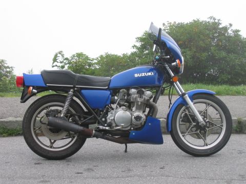 1985 Ford LTD Crown Victoria - A blue Suzuki motorcycle with a windscreen is parked on the side of the road.