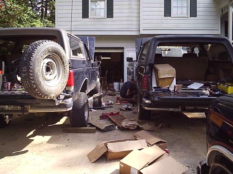 1989 Ford Bronco - Two Ford Bronco SUVs are parked in a driveway, appearing to undergo some maintenance or repair work.