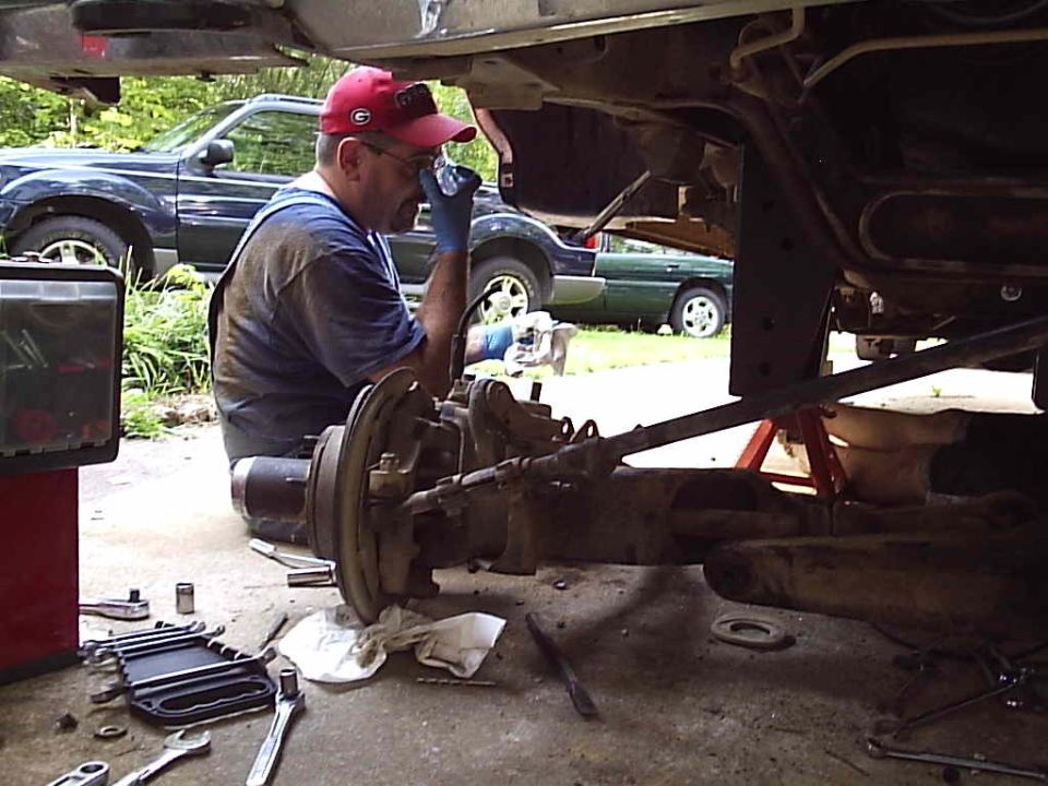 Person working on the exposed front axle and brake rotor of a truck on a jack stand