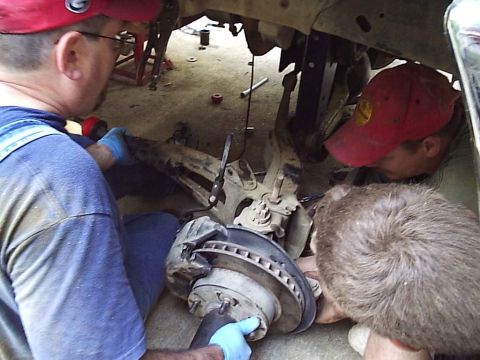 1989 Ford Bronco - Several individuals are gathered around the undercarriage of a vehicle, appearing to perform maintenance on the suspension system.