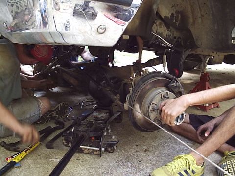 1989 Ford Bronco - Mechanics work on the front suspension of a 1989 Ford Bronco, with a chrome bumper visible above.