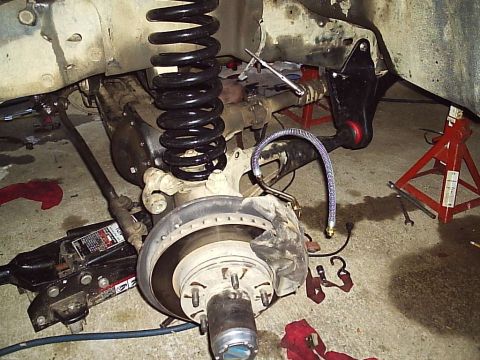 1989 Ford Bronco - Vehicle's front suspension and brake system undergoing maintenance, supported by jack stands.