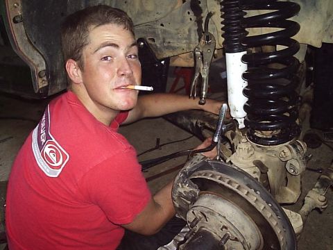 1989 Ford Bronco - A person is working on the suspension of a vehicle, with a cigarette in their mouth.