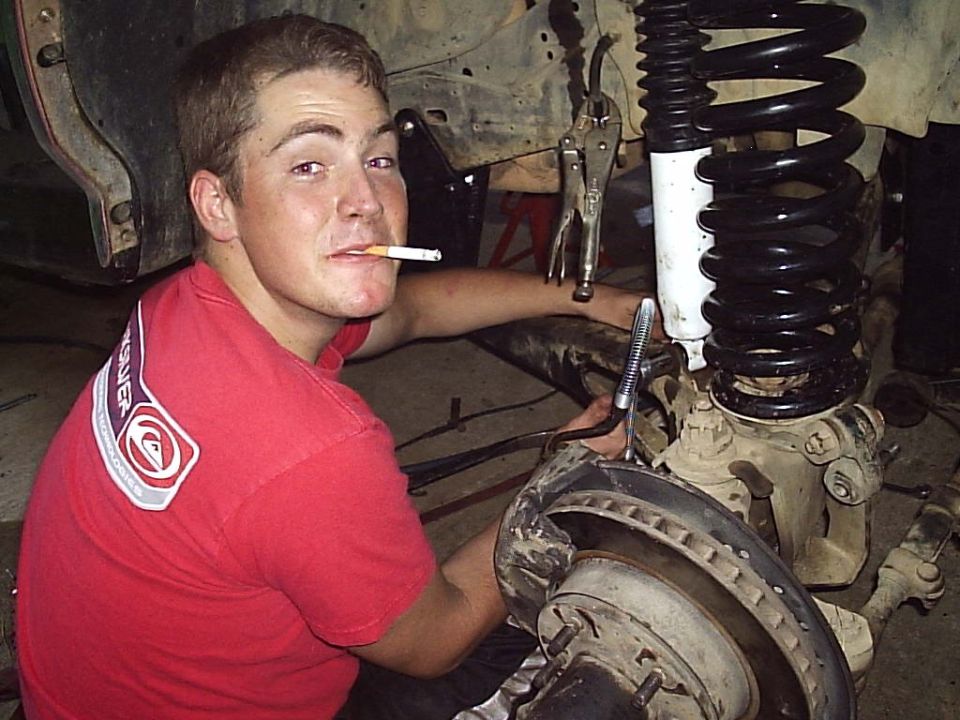guy with cigarette in mouth working on front suspension of off-road vehicle