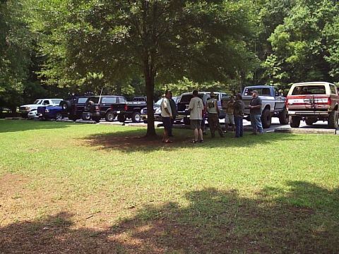 1989 Ford Bronco - A group of trucks and people gathered in a park setting on a sunny day.