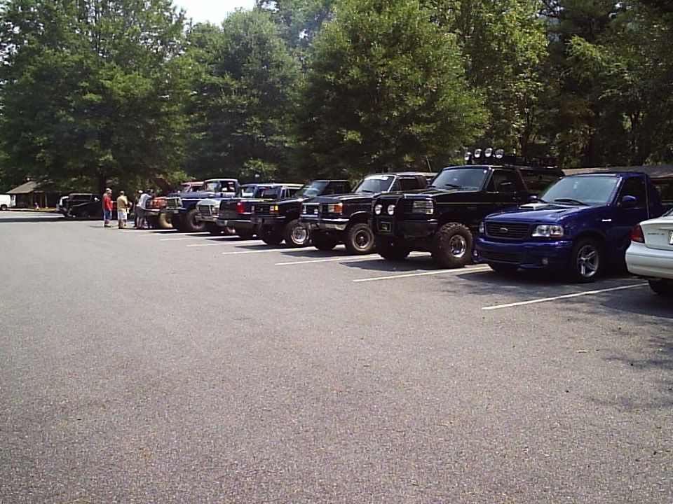 Several trucks and SUVs parked in a lot, some with lifted suspensions and off-road tires