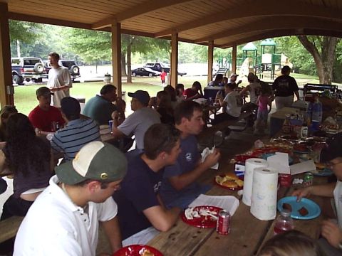 1989 Ford Bronco - A group of people are gathered for a cookout, enjoying food and conversation under a wooden pavilion.