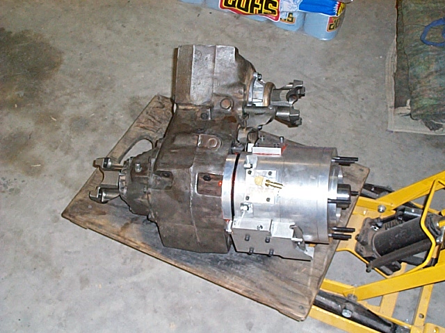 Transfer case bolted to an aluminum gear-reduction unit on plywood beside a trans jack