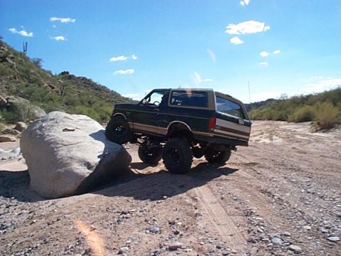1994 Ford Bronco - Ford Bronco attempts to climb over a large rock on a dirt trail in a desert landscape.