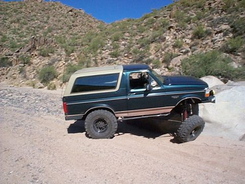 1994 Ford Bronco - This lifted Ford Bronco navigates a rocky desert terrain, its modified suspension clearly visible.