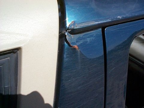 1994 Ford Bronco - The vehicle's door shows significant damage, including a large dent and visible rust.