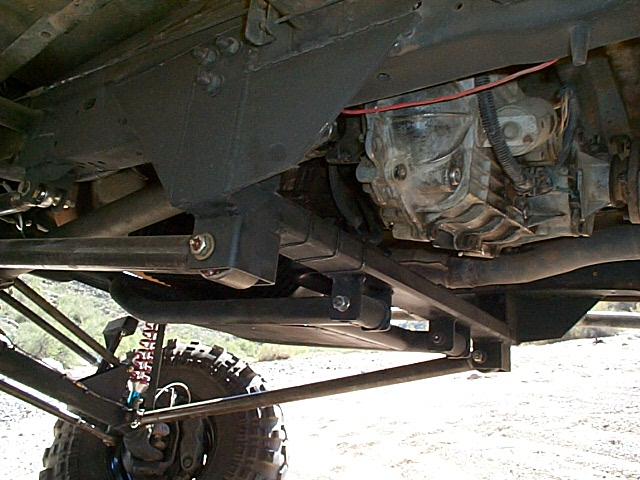 Underbody of a lifted 4x4 showing transfer case, skid plate and red shock