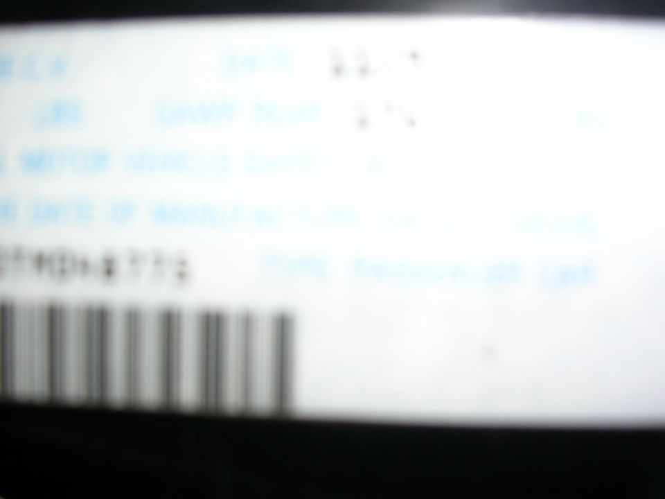 Close-up of a white label with blue text and a barcode. Some text is blurry