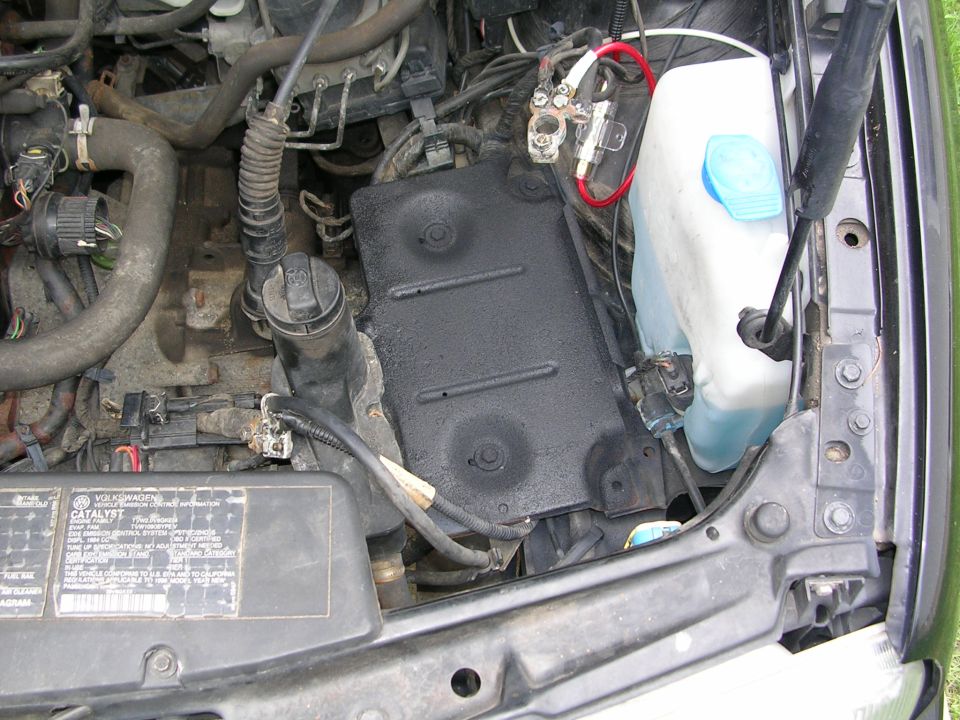 Engine bay with battery terminals, coolant reservoir, and black cover plate