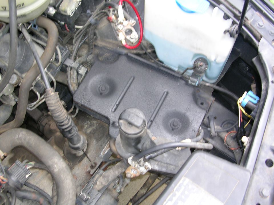 close-up of car engine bay with battery terminals, hoses, and fluid reservoir