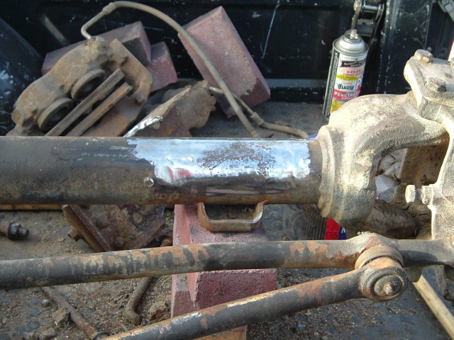 Driveshaft with fresh weld bead clamped over a workbench amid rusty parts