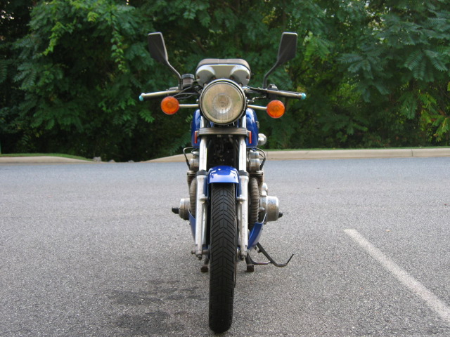 Front view of a blue motorcycle parked on asphalt, with trees in the background