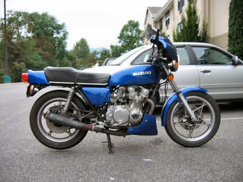 1985 Ford Crown Victoria LTD - A blue Suzuki motorcycle is parked on asphalt with a silver car behind it.