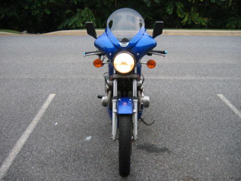 1985 Ford Crown Victoria LTD - A blue motorcycle is parked in a lot, facing the camera with its headlight on.