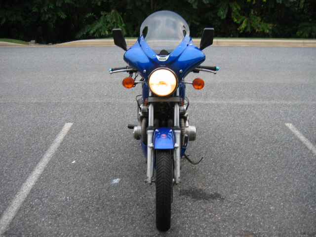 Front view of a blue motorcycle with a clear windshield and round headlight