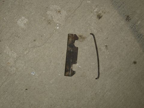 1988 Ford Bronco - Two metal parts, a bracket and a spring, are shown on a concrete floor.