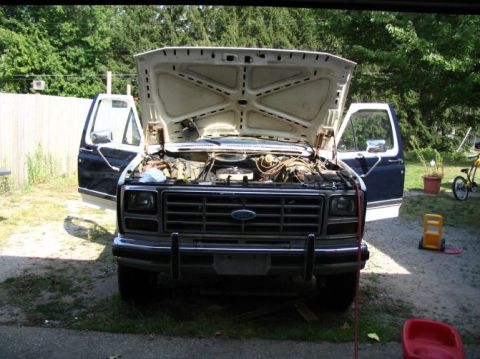 1984 Ford Bronco - Ford truck with hood and doors open, engine exposed. Front view.