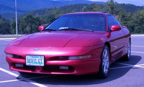 1996 Ford Probe - A red 1996 Ford Probe is shown from the front in a parking lot with trees and hills in the background.