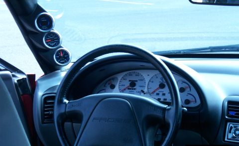 1996 Ford Probe - The dashboard of a car features a steering wheel and instrument cluster, with additional gauges mounted on the A-pillar.
