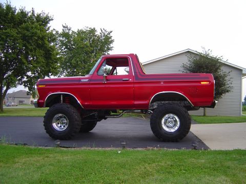 1978 Ford Bronco - A red 1978 Ford Bronco with a significant suspension lift, chrome slotted wheels and large off-road mud tires, shown in profile parked on a…