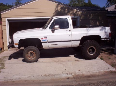 1988 Ford Bronco - A white pickup truck with off-road tires is parked on a concrete driveway in front of a garage.