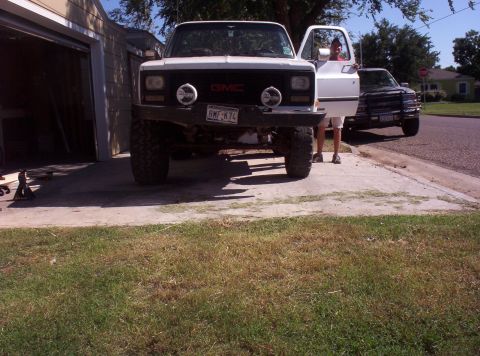 1988 Ford Bronco - A white GMC pickup truck is parked in front of a garage, with another truck visible in the background.