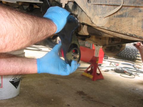 1988 Ford Bronco - Mechanic's hands in blue gloves work on installing a suspension part on the underside of a vehicle.