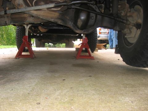 1988 Ford Bronco - The underside of a vehicle is elevated on jack stands, revealing its mechanical components and suspension system.